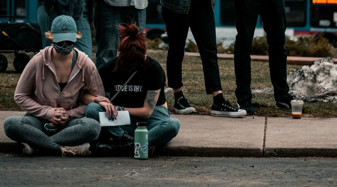 Two people sit solemnly on a street curb during a gun violence protest