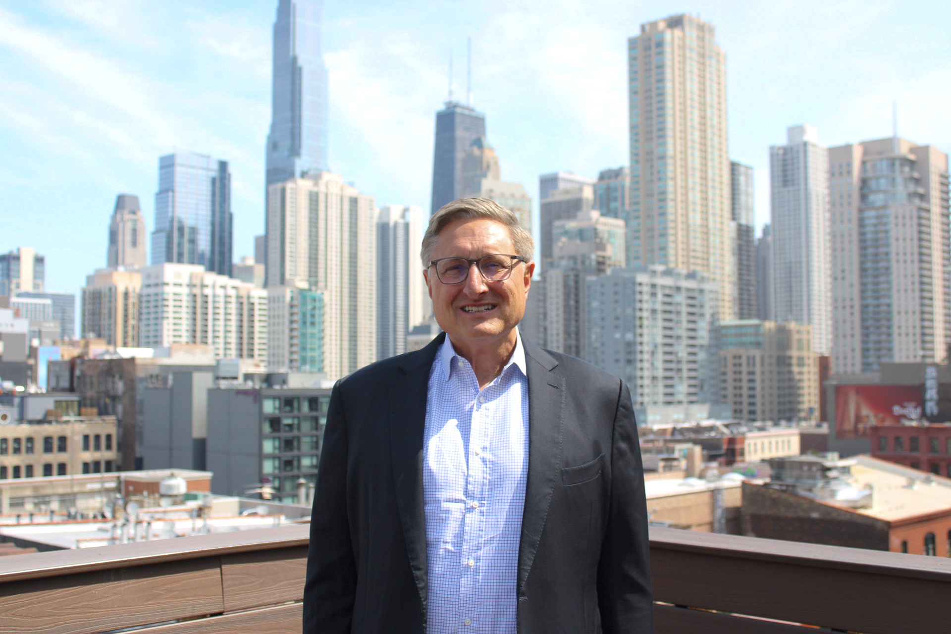 AMOpportunities new CEO John Danaher poses on a rooftop, the Chicago skyline behind him